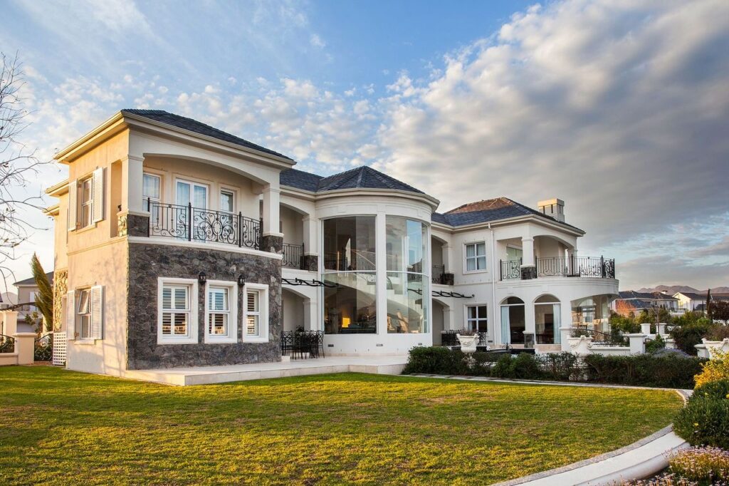 A beautiful luxury Mansion with modern aluminum windows painted white with lots of glass for natural light and a green front lawn in Cape Town